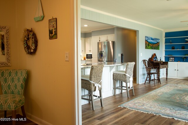 interior space featuring a kitchen breakfast bar, wood finished floors, crown molding, and stainless steel fridge