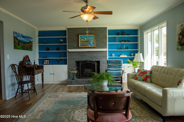 living room featuring crown molding, built in features, a ceiling fan, wood finished floors, and a brick fireplace