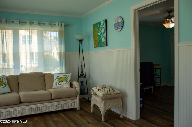 living room featuring crown molding, a wainscoted wall, ceiling fan, and dark wood finished floors