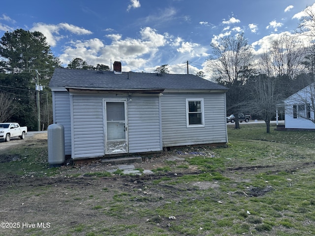 back of house featuring roof with shingles, a yard, and a chimney