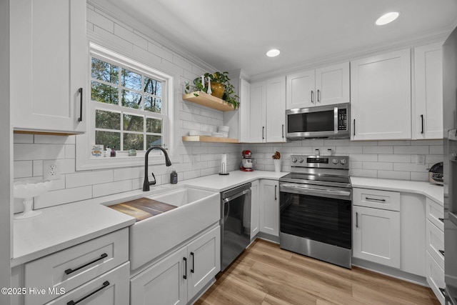 kitchen with white cabinets, decorative backsplash, stainless steel appliances, light wood-style floors, and a sink