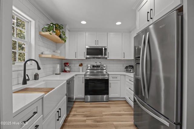 kitchen with light countertops, appliances with stainless steel finishes, open shelves, and light wood-style floors