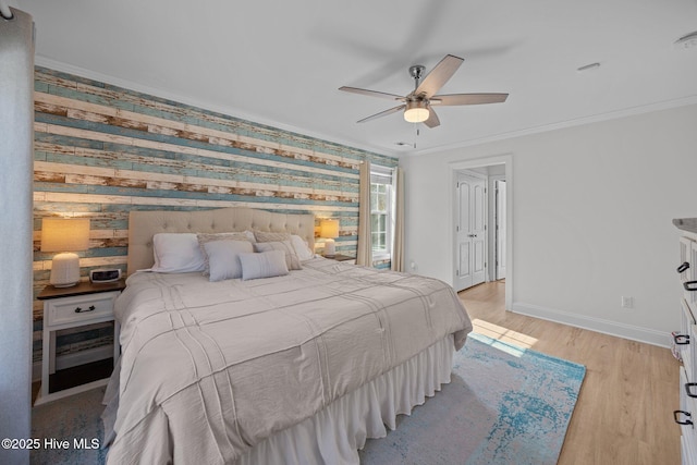 bedroom featuring baseboards, an accent wall, ornamental molding, and light wood-style flooring