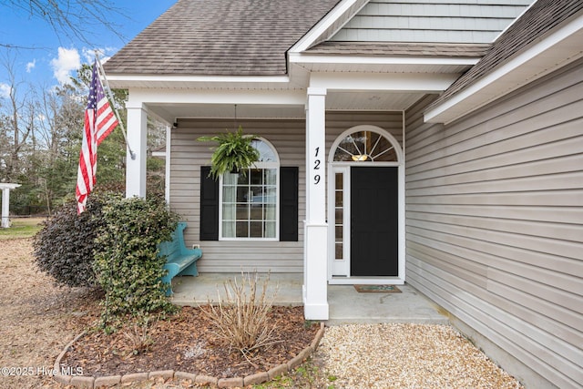 doorway to property featuring a porch and roof with shingles