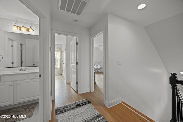 hallway featuring baseboards, visible vents, an upstairs landing, light wood-style floors, and a sink