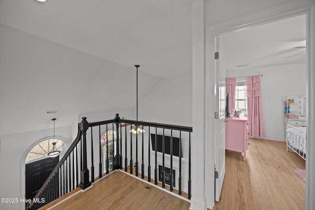 hallway with a notable chandelier, wood finished floors, an upstairs landing, visible vents, and vaulted ceiling