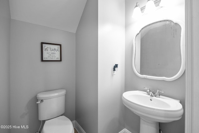 half bathroom with toilet, vaulted ceiling, and a sink