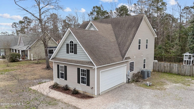 view of side of home with central AC unit, a garage, fence, roof with shingles, and gravel driveway