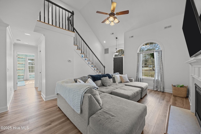 living room with visible vents, a fireplace with flush hearth, light wood-style flooring, stairway, and high vaulted ceiling