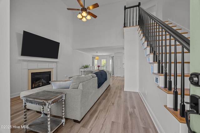 living room with a glass covered fireplace, stairway, wood finished floors, and baseboards