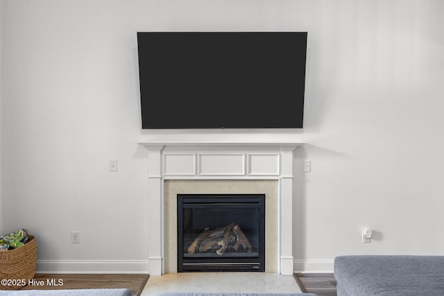 interior details with wood finished floors, a glass covered fireplace, and baseboards