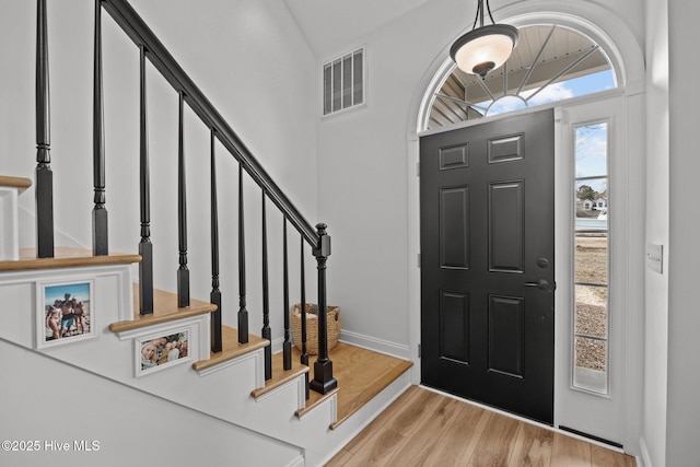 foyer entrance featuring visible vents, a towering ceiling, wood finished floors, baseboards, and stairs