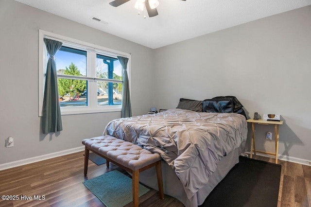 bedroom with a ceiling fan, visible vents, baseboards, and wood finished floors