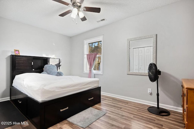 bedroom with a textured ceiling, wood finished floors, visible vents, and baseboards