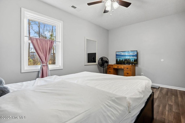 bedroom featuring dark wood finished floors, visible vents, ceiling fan, a textured ceiling, and baseboards