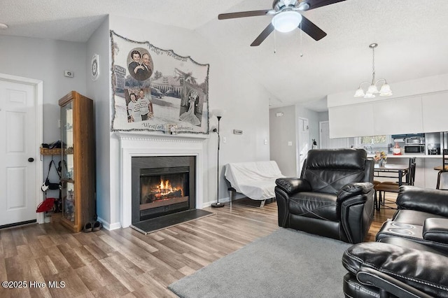 living area with a glass covered fireplace, wood finished floors, vaulted ceiling, a textured ceiling, and ceiling fan with notable chandelier