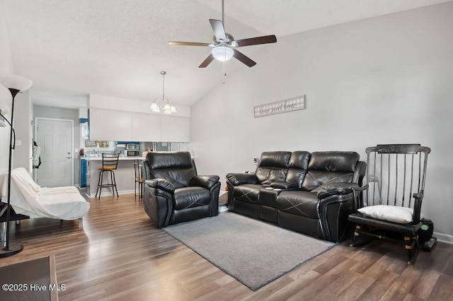 living area with baseboards, high vaulted ceiling, wood finished floors, and ceiling fan with notable chandelier