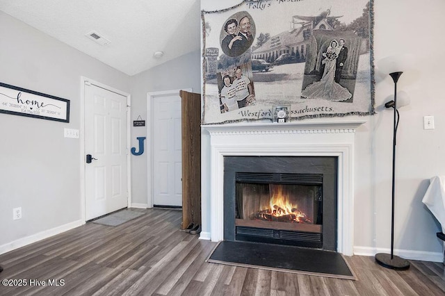 interior space with a fireplace with flush hearth, visible vents, baseboards, and wood finished floors