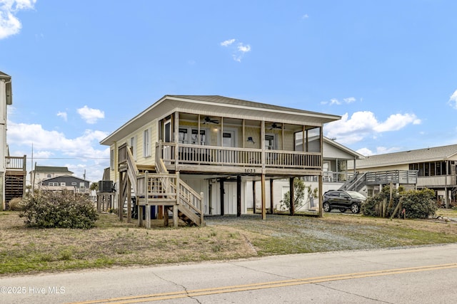 coastal home with a carport, a ceiling fan, driveway, and stairs