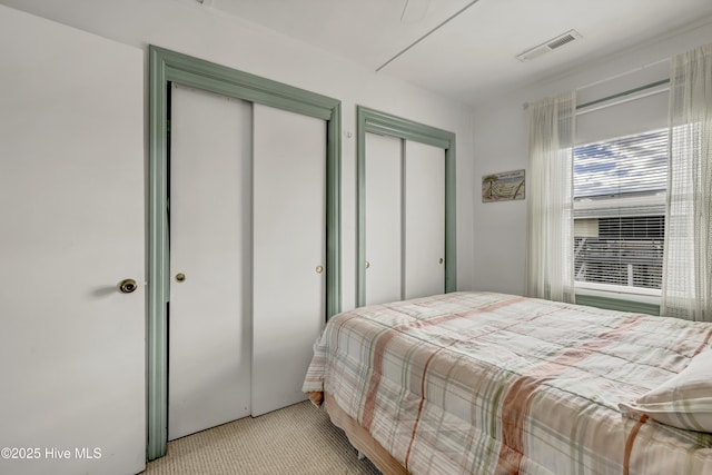 bedroom featuring carpet floors, visible vents, and two closets