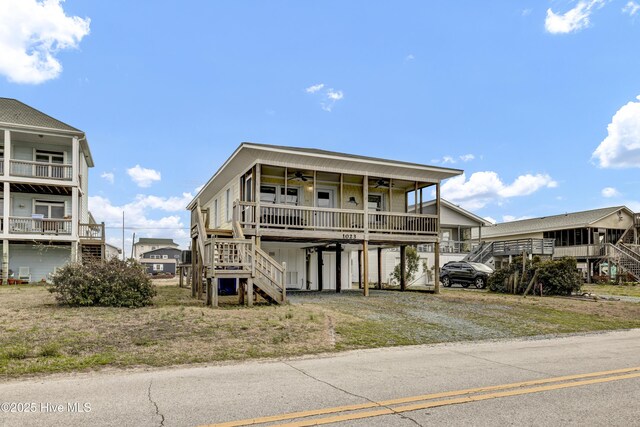 coastal inspired home featuring dirt driveway, ceiling fan, a carport, and stairs