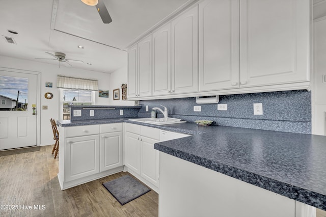 kitchen featuring dark countertops, a peninsula, light wood-style floors, white cabinetry, and a sink