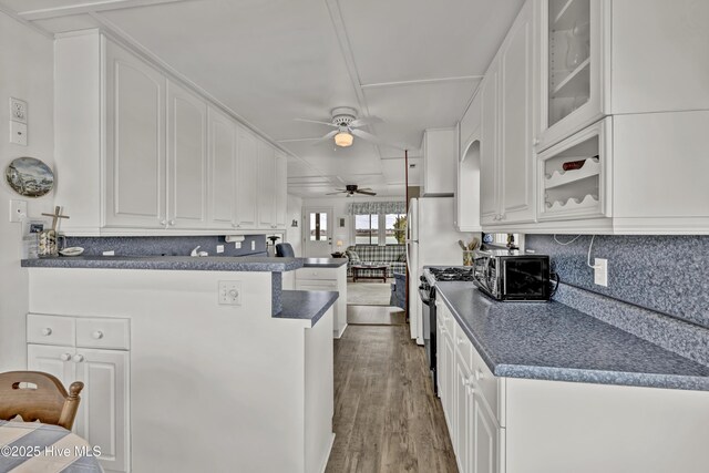 kitchen featuring a peninsula, white cabinetry, black range with gas stovetop, dark countertops, and glass insert cabinets