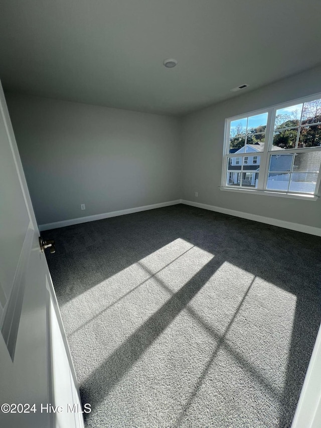 unfurnished room with dark colored carpet, visible vents, and baseboards