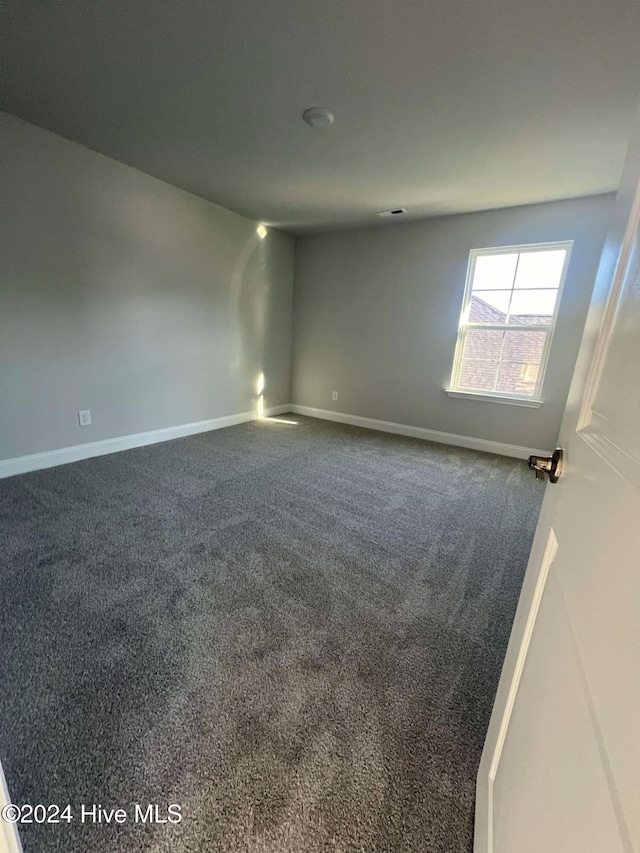 empty room featuring dark colored carpet and baseboards