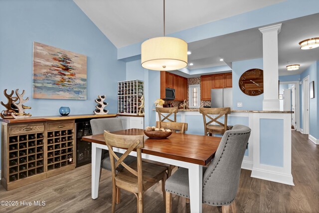 dining room featuring beverage cooler, lofted ceiling, decorative columns, recessed lighting, and wood finished floors