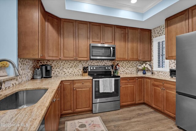 kitchen with light wood-type flooring, brown cabinets, a sink, appliances with stainless steel finishes, and a raised ceiling