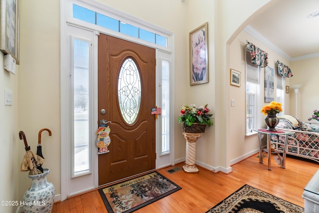 foyer entrance featuring wood finished floors, visible vents, arched walkways, and ornamental molding