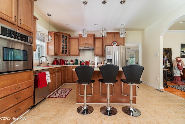 kitchen featuring a sink, brown cabinets, under cabinet range hood, and stainless steel appliances