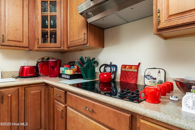 kitchen with light countertops, black electric stovetop, brown cabinets, and under cabinet range hood