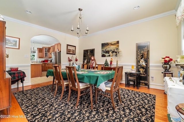 dining space featuring a wainscoted wall, crown molding, light wood-style floors, and arched walkways