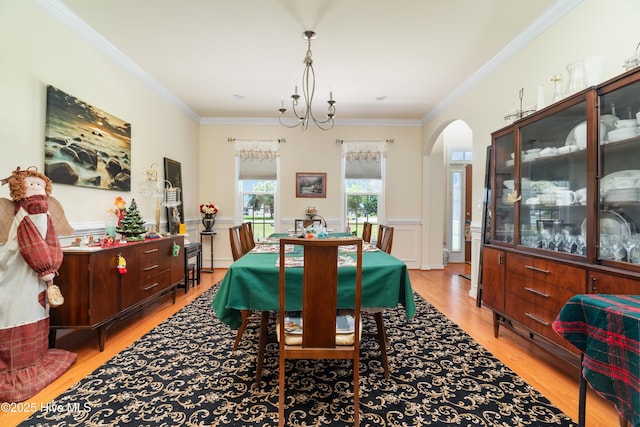 dining space featuring a wainscoted wall, arched walkways, ornamental molding, light wood-type flooring, and a chandelier