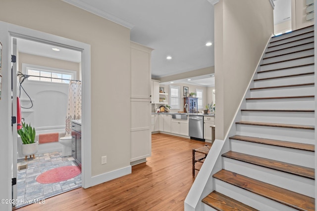 entryway with stairs, light wood-type flooring, a wealth of natural light, and crown molding