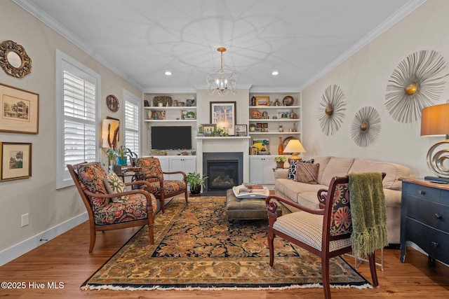 living area with built in features, ornamental molding, wood finished floors, a chandelier, and baseboards