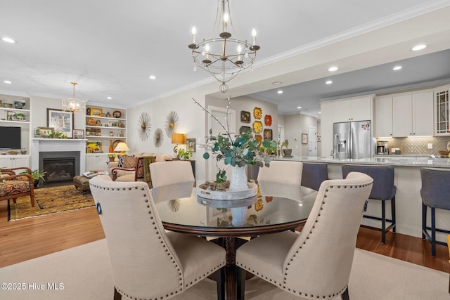 dining area featuring light wood-type flooring, an inviting chandelier, a fireplace, and ornamental molding