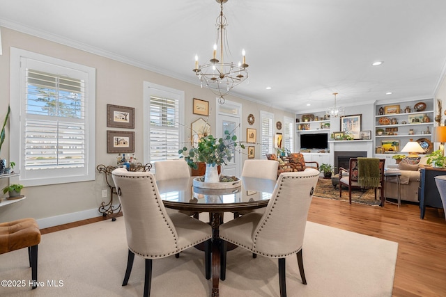 dining area with light wood finished floors, ornamental molding, a fireplace, and a chandelier
