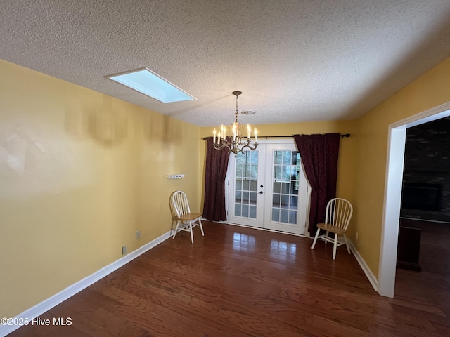 unfurnished dining area featuring baseboards, a chandelier, french doors, a skylight, and wood finished floors