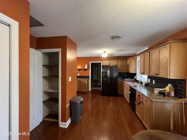 kitchen with visible vents, a sink, black appliances, dark wood-type flooring, and tasteful backsplash