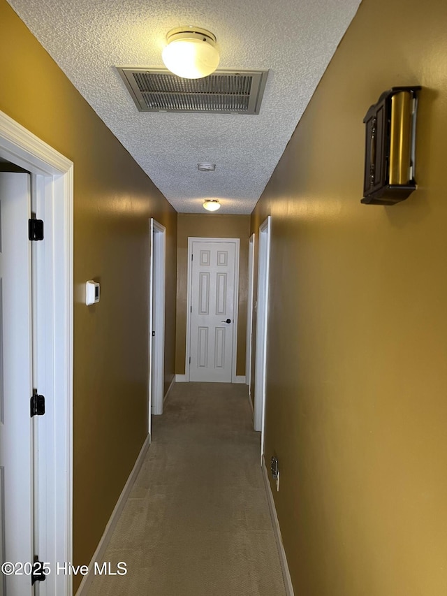 hallway featuring baseboards, light colored carpet, visible vents, and a textured ceiling