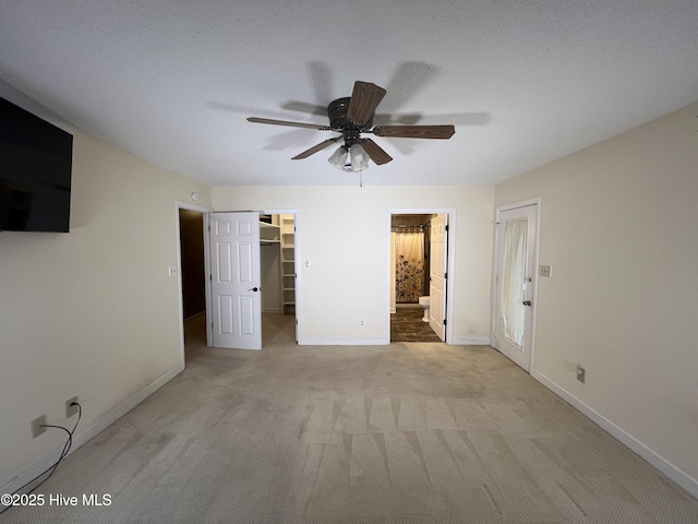 unfurnished bedroom featuring baseboards, a spacious closet, a closet, light colored carpet, and connected bathroom