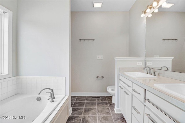 bathroom with double vanity, toilet, a sink, baseboards, and a bath