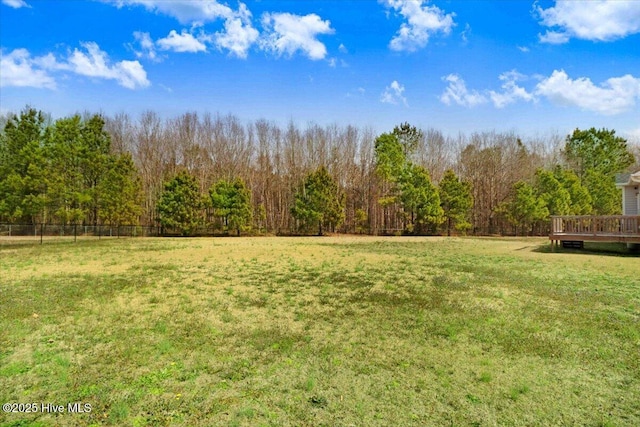 view of yard with fence, a deck, and a forest view