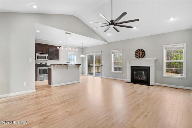 unfurnished living room with light wood-style floors, a wealth of natural light, ceiling fan, and a fireplace with flush hearth