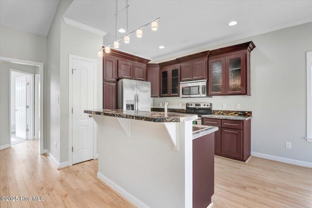 kitchen featuring light wood finished floors, glass insert cabinets, appliances with stainless steel finishes, a breakfast bar area, and crown molding