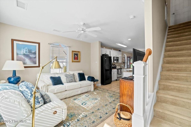 living area with ceiling fan, light wood finished floors, stairway, and visible vents