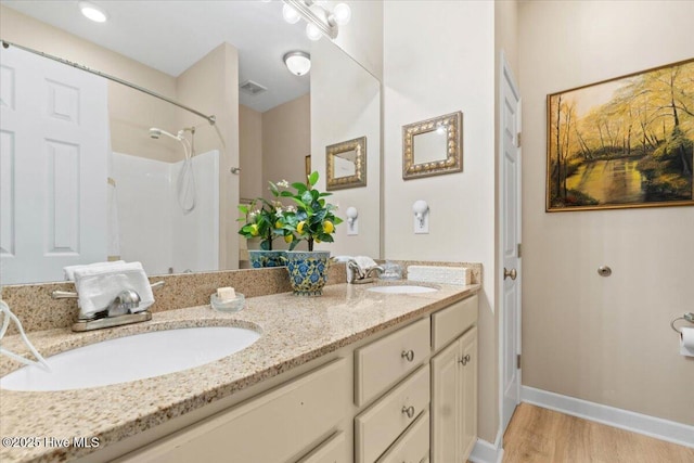 full bathroom featuring double vanity, walk in shower, a sink, and wood finished floors